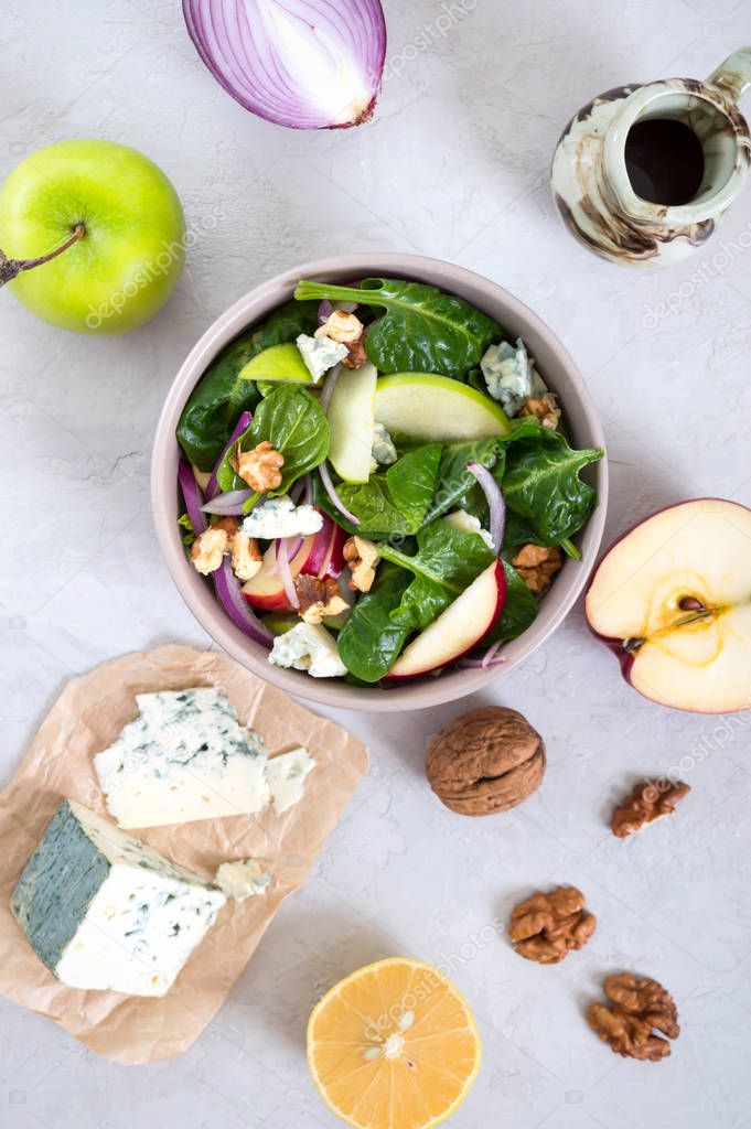 Delicious diet fitness salad with spinach, apples, red onions, blue cheese, nuts. Proper nutrition. Light concrete background. Top view.