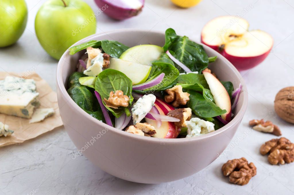 Delicious diet fitness salad with spinach, apples, red onions, blue cheese, nuts. Proper nutrition. Light concrete background.