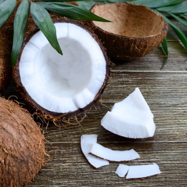 Hindistan cevizi. Tam hindistan cevizi, kabuk, hindistan cevizi gevreği ve ahşap arka planda yeşil yapraklar. Büyük kaçık. Kabuğunda tropik meyve hindistan cevizi. Spa mı? Yemek fotoğrafı. Doku tropikal meyvesi.