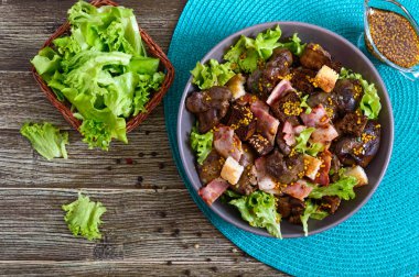 Sağlıklı tavuk ciğeri salatası, çavdar ekmeği, füme domuz pastırması, yeşil salata ve ahşap arka planda hardal sosu. Üst görünüm.