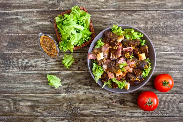 Warm healthy salad of chicken liver, rye croutons, smoked bacon, green salad and mustard sauce in a bowl on a wooden background