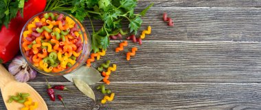 Cavatappi, cam kavanozda çiğ makarna, taze sebzeler, ahşap arka planda yeşiller. Makarna kolorata. Sebzeli makarna. Dirsek makarna. Boşluğu kopyala.