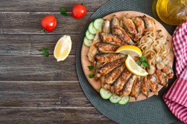 Kızarmış kapelin, sprat. Ahşap bir arka planda tabakta küçük kızarmış balık. Üst görünüm.