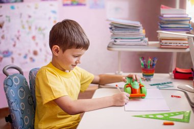 Çocuk ev ödevi yapıyor ve evde en sevdiği oyuncağıyla oynuyor. Evde öğrenme, kendini karantina konsepti. Koronavirüs salgını. Kendini izole etme, ev karantinası. Evde uzaklık öğrenimi.