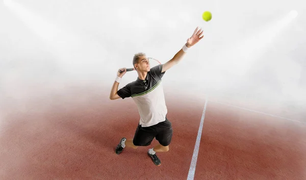 Junger Mann spielt Tennis auf orangefarbenem Platz im Morgennebel — Stockfoto