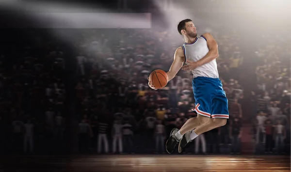 Баскетболист прыгает с мячом на стадионе в огнях — стоковое фото