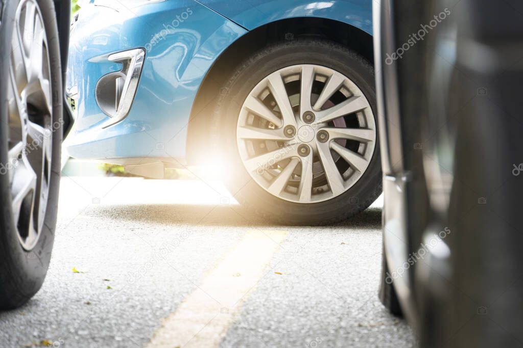 Luxury blue car parked in garage. There are blurry images of two cars in the front. Sunlight shines from the back through the wheel.