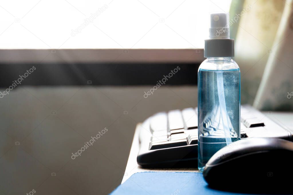 Alcohol spray bottle placed on a computer desk with the light from the window. Concept work from home fir fighting coronavirus.