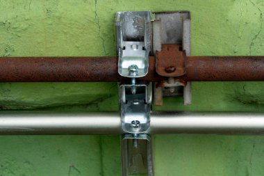 Duvardaki boru kilidi kıskacındaki Orta Yol Teknolojisi devrede. Pas lekeli eski borular Ve yeni temiz borular.