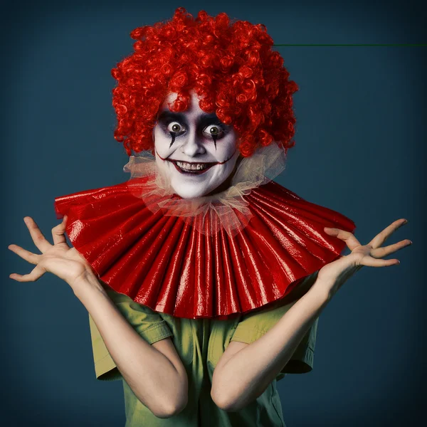 Fille folle dans un costume terrible clown dans une perruque rouge et vorotkike rouge et chemise verte sur un fond bleu. Halloween . — Photo