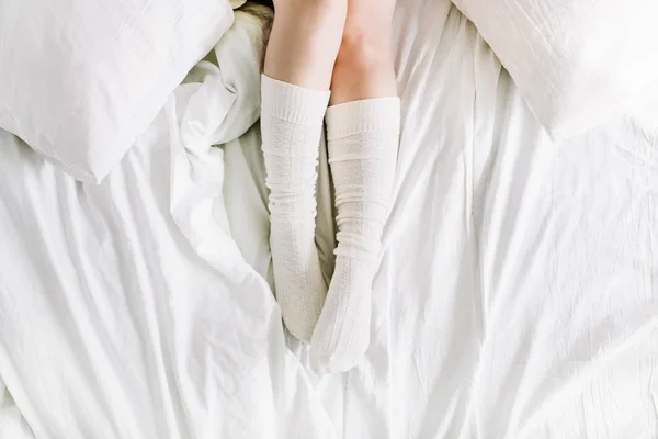 Pernas femininas na cama com roupa de cama branca — Fotografia de Stock