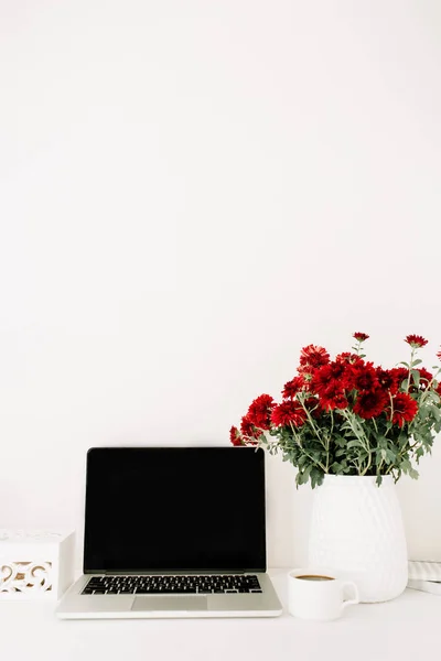 Office desk with laptop and beautiful red flowers bouquet — Stock Photo, Image