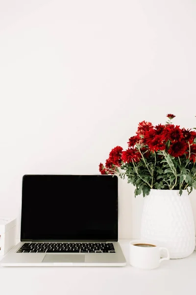 Γραφείο με φορητό υπολογιστή και όμορφα κόκκινα λουλούδια μπουκέτο — Φωτογραφία Αρχείου