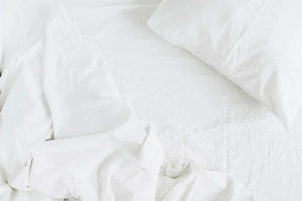 Flat lay of white bed with pillows, blanket and sheet. Top view minimal linen concept.