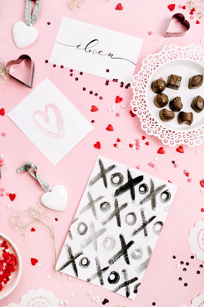 Valentine's Day or Love composition. Chocolate candies, heat symbols, cards on pale pink background. Flat lay, top view.