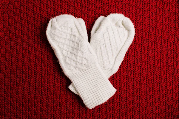White knitted mittens on red knitted background. Winter minimal background. Flat lay, top view heart symbol. Valentine\'s Day concept.