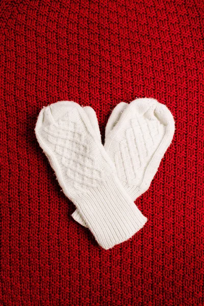 Knitted mittens on red knitted background. Winter minimal background. Flat lay, top view heart symbol.