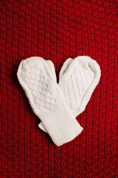 White knitted mittens on red knitted background. Winter minimal background. Flat lay, top view heart symbol. Valentine\'s Day concept.