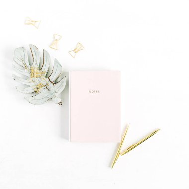 Soluk pastel pembe defter, altın kalem ve klipleri, monstera palmiye yaprağı dekorasyon beyaz arka plan üzerinde. Düz yatıyordu, en iyi görünüm ev ofis Resepsiyon kavramı.
