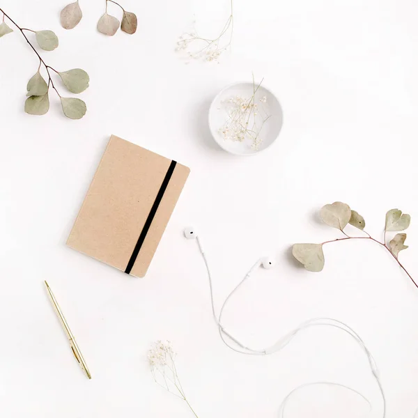 Home office desk with craft diary, pen, headphones and eucalyptus branches on white background. Flat lay, top view.