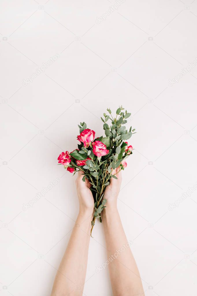 Woman hands hold rose flowers and eucalyptus branch bouquet. Flat lay, top view spring background.