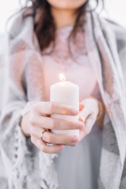 Genç kadın elinde mum ile gri battaniyeye sarılmış.