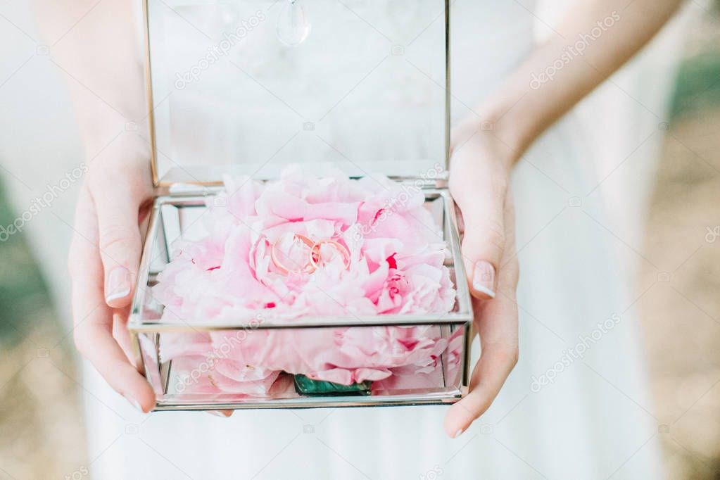 Bride holding glass casket with peony flower buds and wedding rings. Bridal fashion background.