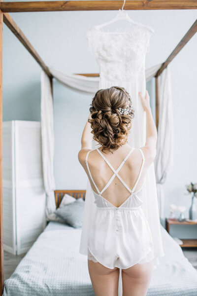 Молодая красивая невеста в нижнем белье трогает свадебное платье. Свадебная модная композиция
.