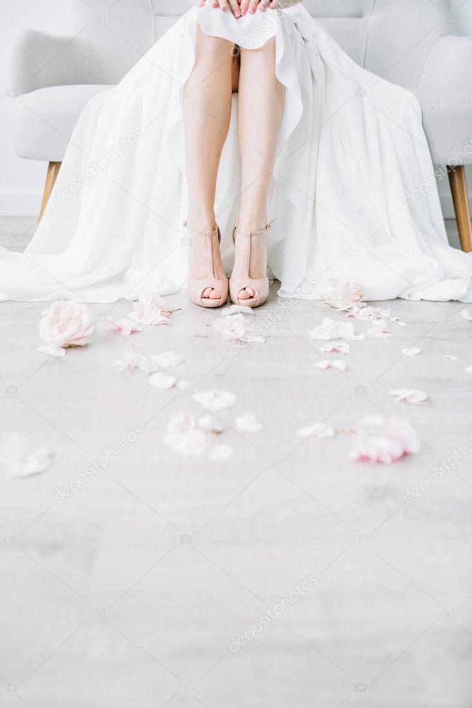 Young bride legs in pink high heel shoes and pink flower petals. Festive wedding fashion concept.