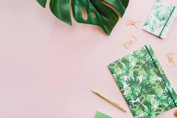 Egzotik tropik monstera palmiye yaprağı ve Ev Ofis Kırtasiye soluk pembe bir arka plan üzerinde. Düz yatıyordu, en iyi görünüm çok az çalışma alanı.