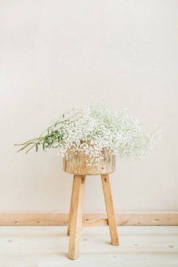 Gypsophila çiçek buketi ahşap Stool'da soluk pastel bej renkli arka plan üzerinde beyaz. En az yaşam tarzı kavramı.