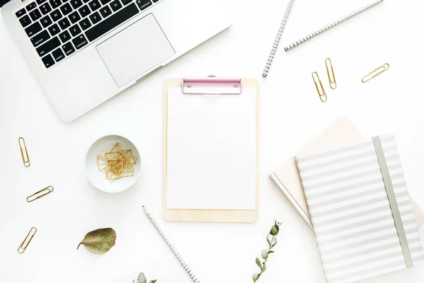 Flat lay office workspace with blank clipboard, laptop and stationery on white background. Top view minimal mock up template concept.