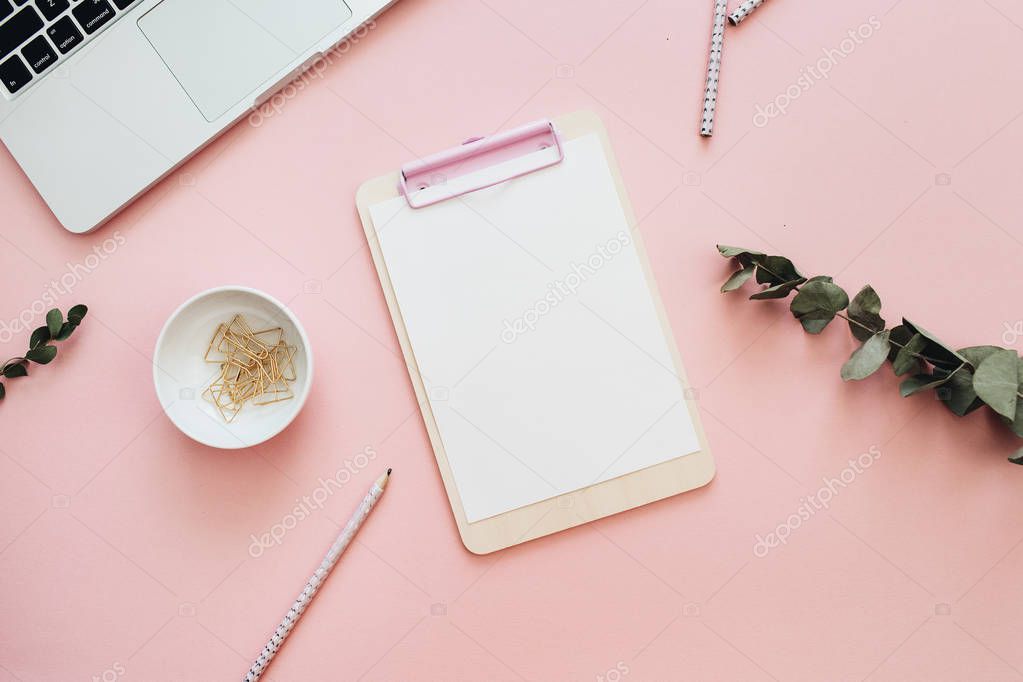 Flat lay home office desk workspace with laptop, clipboard and eucalyptus branches on pastel pink background. Top view minimal mock up template.