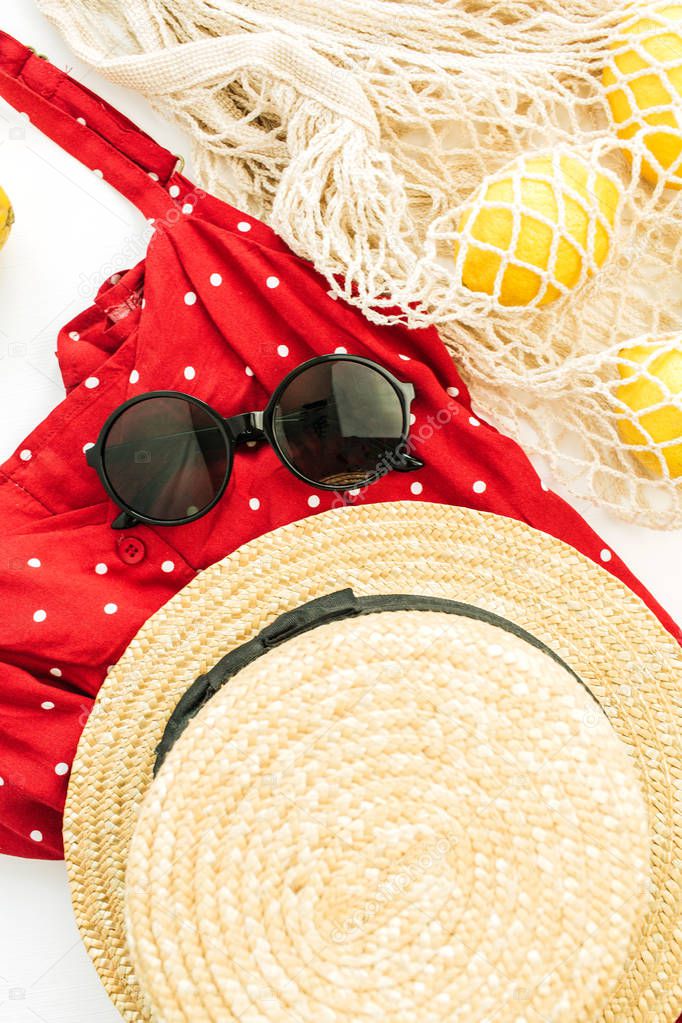 Summer female fashion composition. Red dress, straw, string bag, sunglasses and lemons. Flat lay, top view.