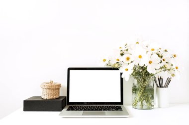 İş, serbest çalışma, blog yazarı konsepti. Model yap, boş, kopyala alanı. Diz üstü bilgisayar beyaz masanın üzerinde vazoda papatyalar, siyah kutu, saman sepet ile beyaz duvara karşı duruyor.. 