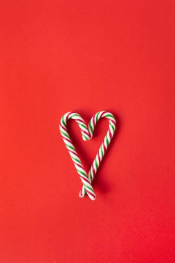 Noel / Yeni Yıl kompozisyonu. Kırmızı arka planda şeker çubuklarından yapılmış kalp sembolü. Düz konum, üst görünüm yaratıcı festival konsepti.