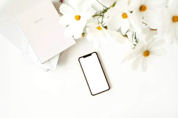 Business, freelance, blogger concept. Mock up, empty, copy space. Mobile phone on white table with daisies and notebooks.