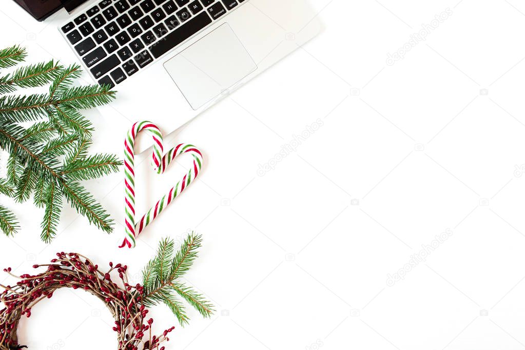 Christmas / New Year holiday composition. Home office desk with laptop, Christmas baubles / balls, fir branches, candy sticks on white background. Flat lay, top view festive business concept.