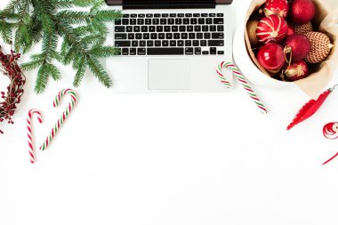 Noel / Yeni Yıl bayramı kompozisyonu. Bilgisayarlı ofis masası çalışma alanı, Noel mücevherleri / topları, köknar dalları, beyaz arka planda şeker çubukları. Düz yatar, üst görünüm, şenlik kahramanı başlığı.