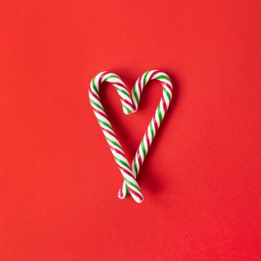 Noel / Yeni Yıl kompozisyonu. Kırmızı arka planda şeker çubuklarından yapılmış kalp sembolü. Düz konum, üst görünüm yaratıcı festival konsepti.