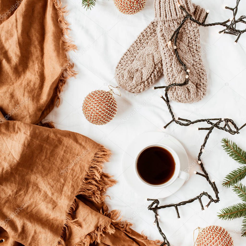 Christmas / New Year composition. Knitted mittens, coffee cup, garland, fir branches, Christmas baubles, ginger plaid on white blanket. Flat lay, top view decorated holiday background.
