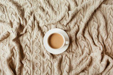 Bej örülmüş ekose battaniyeli bir fincan sütlü kahve. Düz yatış, üst manzara natürmort sabah kahvaltısı konsepti.