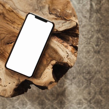 Boş ekran akıllı telefon. Saf ahşap tabure ve halının üzerinde boş bir kopya alanı var. Düz konum, sosyal medya, web sitesi, dergi için üst görünüm şablonu.