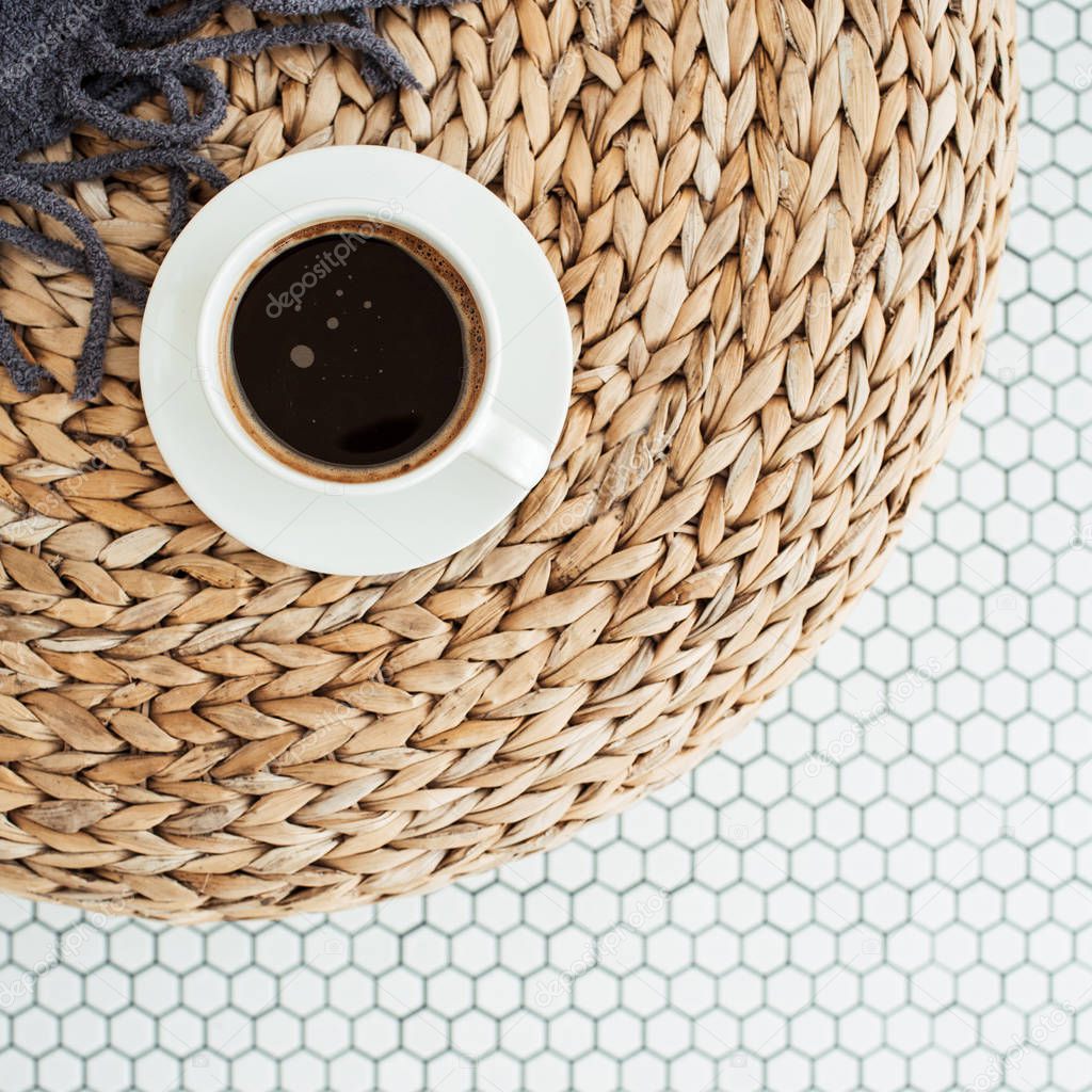 Flat lay cup of coffee, plaid blanket on rattan straw puff on white mosaic tile. Morning breakfast. Minimal modern interior design concept. Top view.