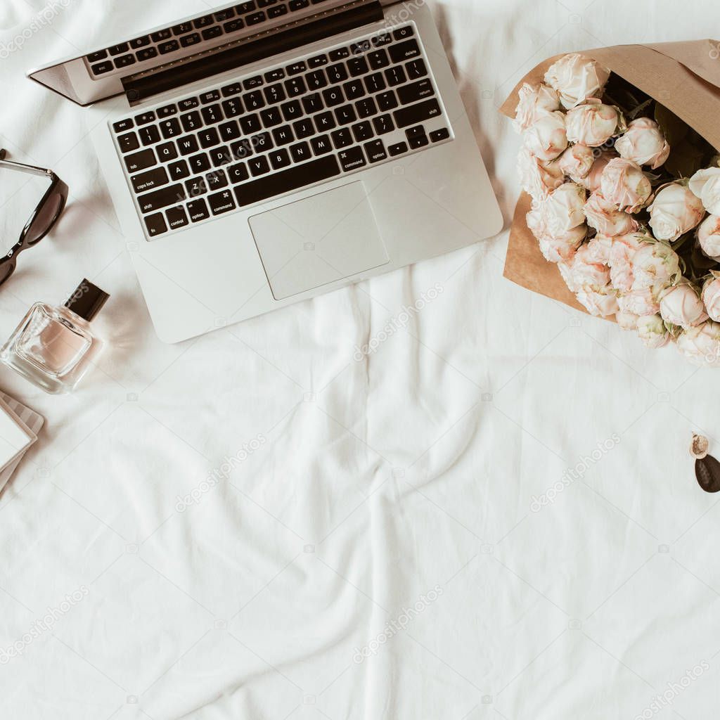 Fashion, beauty, lifestyle blogger home office workspace. Laptop, roses bouquet, women's accessories on white linen. Flat lay, top view woman work concept.