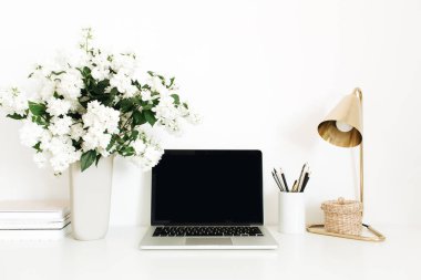 Masasında boş kopya alanı olan bir dizüstü bilgisayar. Ofis masası çalışma alanı, çiçek buketi, masa lambası. Asgari serbest çalışma konsepti.