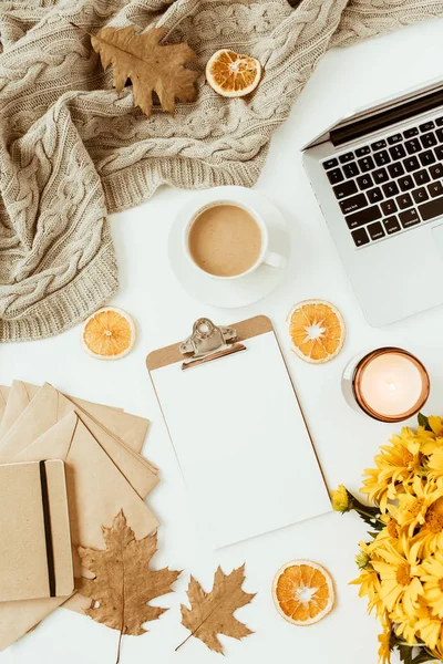 Flat lay home office table desk workspace with blank copy space clipboard, flowers bouquet, coffee cup, blanket, envelopes, leaves on white background. Top view girl boss business, work concept.