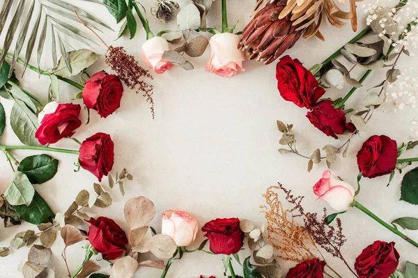 Round frame border of pink, red rose flowers, protea, tropical palm leaf, eucalyptus on beige background. Mockup blank copy space. Flat lay, top view floral composition.
