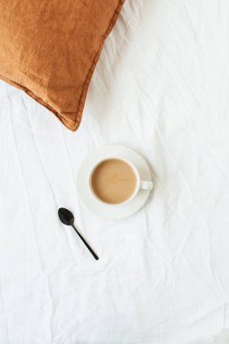 Sütlü, siyah kaşıklı, beyaz çarşaflı, zencefilli bir fincan kahve. Durgun bir hayat, yaşam tarzı, minimum sabah kahvaltısı konsepti. Üst görünüm modern iç tasarım.