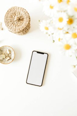 Boş kopya alanı olan akıllı telefon. Beyaz arka planda papatya çiçeği buketi olan ofis masası çalışma alanı. Düz konum, üst görünüm serbest yazar konsepti.